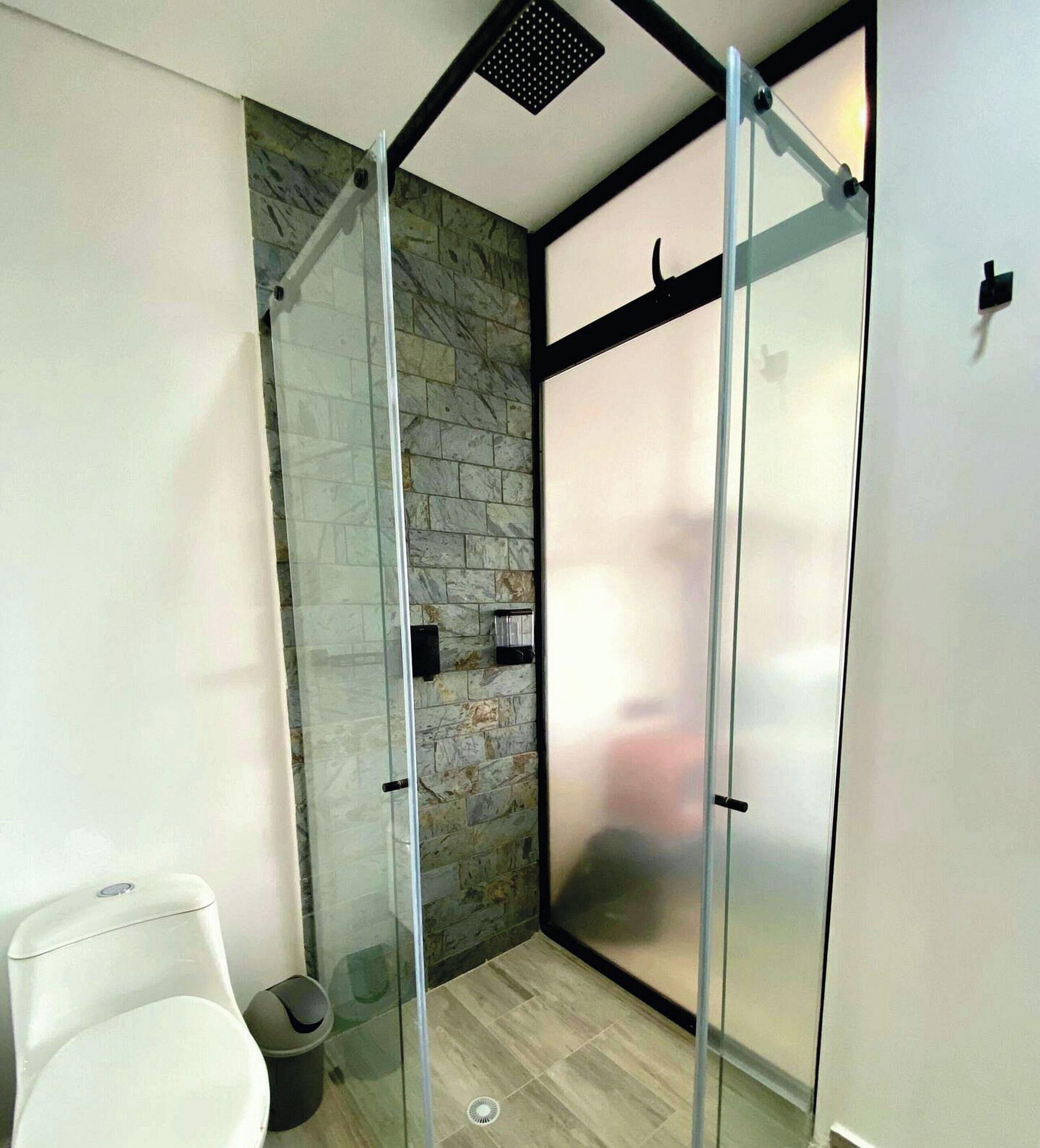 A modern bathroom with a glass shower enclosure, stone wall, and a white toilet.