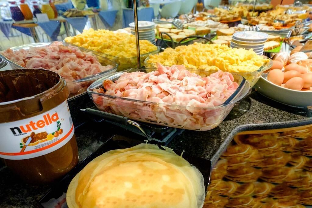 A buffet with various food items including ham, scrambled eggs, and a Nutella jar.