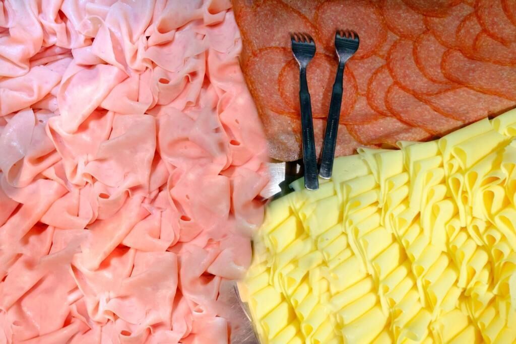 A close-up of various food items, including pink and yellow processed meats, arranged on a tray.