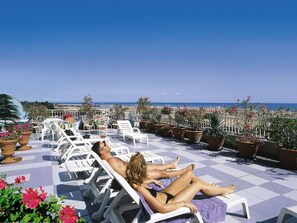 A sunbathing area with lounge chairs and potted plants, overlooking a beach. - Hotel Miramare Bibione  (Bibione)