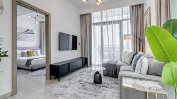 A modern hotel room with a bed, a sofa, a TV, a coffee table, and a large window with curtains.