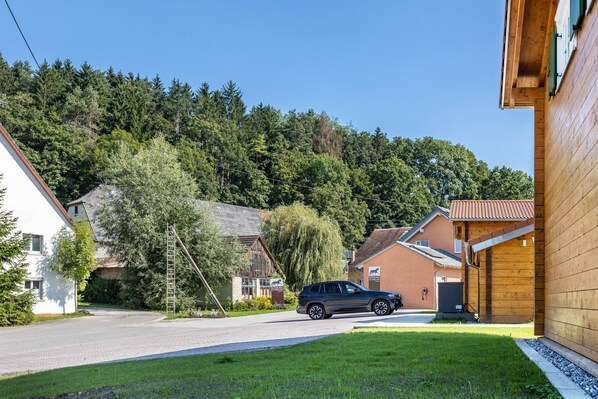 A residential street with houses, a car, and a forested hill in the background.