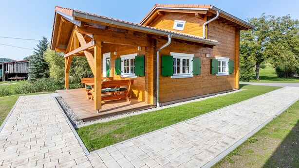 Eine Holzhütte mit verdeckter Veranda, einem Pflasterweg und einem grünen Rasen.