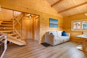 Interior de una cabaña de madera con escalera, sofá, mesa y un cuadro de un paisaje.