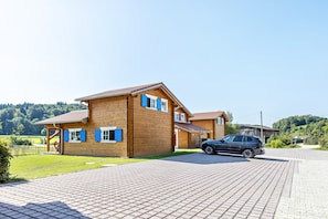 Uma casa de madeira de dois andares, com entrada pavimentada e um carro estacionado.