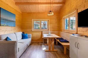 Interior de uma cabana de madeira com sofá, mesa, banco e televisão.