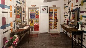 A hallway with patterned walls, a wooden bench, a door with a numbered plaque, and a welcome mat. - Bonjourla Otel (Urla)