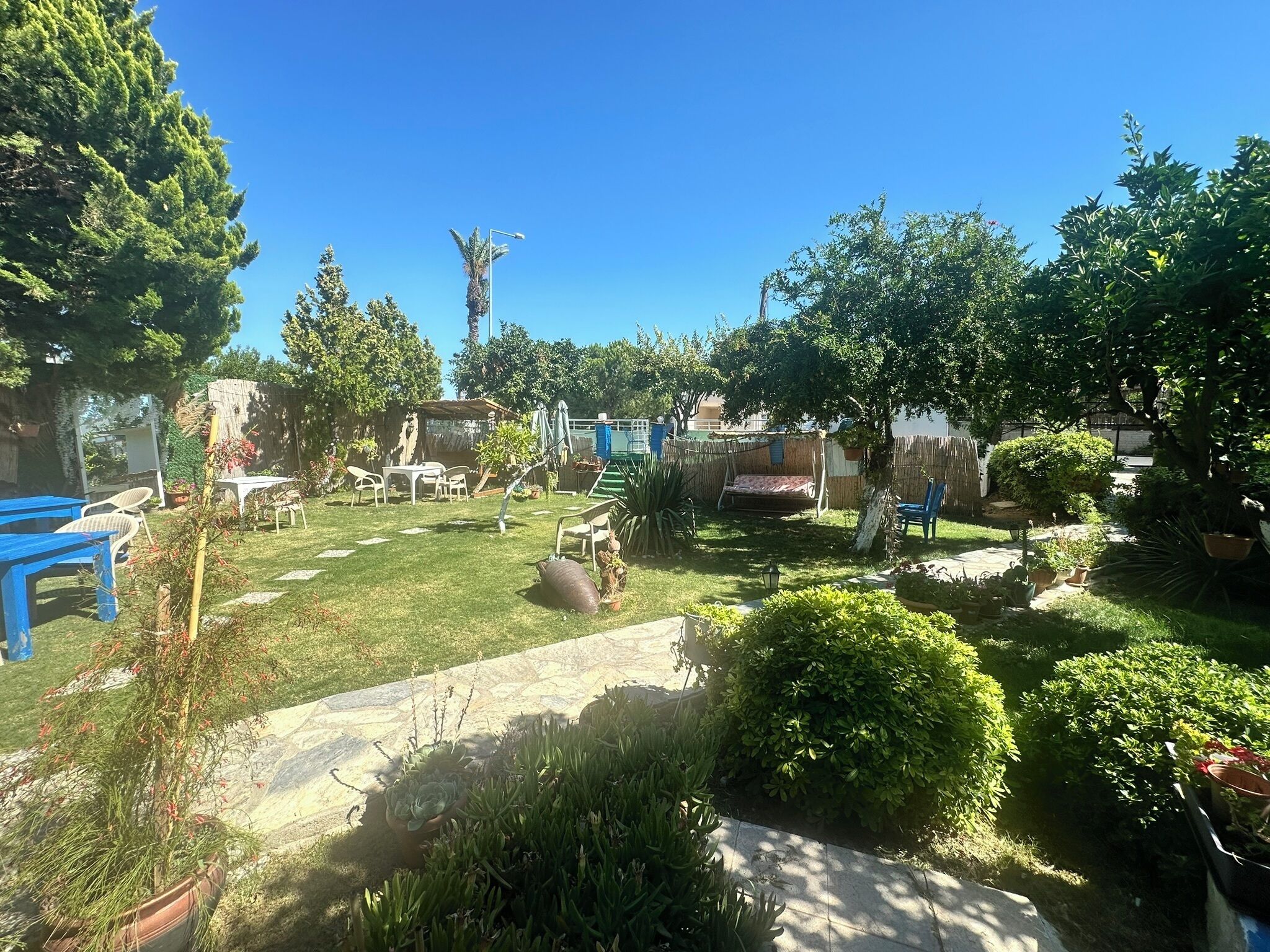 Un jardín bien cuidado con diversas plantas y un área de descanso con mesas y sillas.