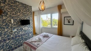 A bedroom with a patterned wall, a bed with white linens, a mounted TV, and a window with curtains. - Bonjourla Otel (Urla)