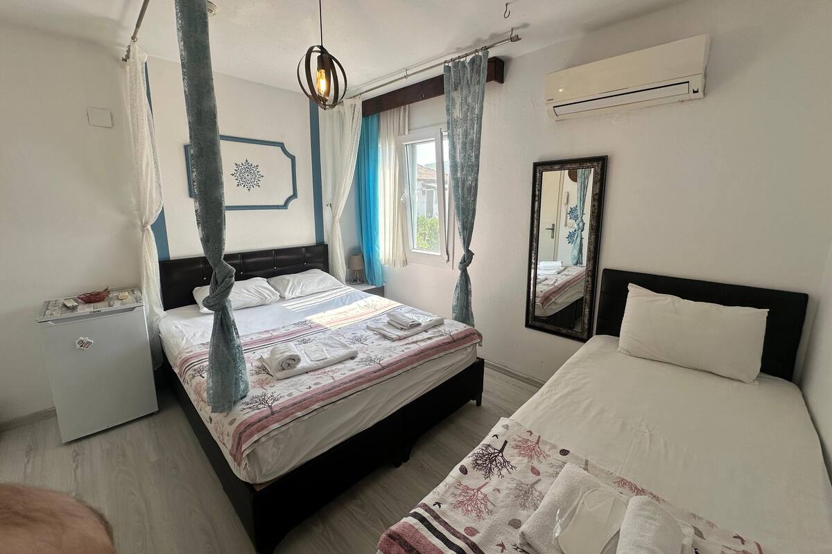 A bedroom with a four-poster bed, a single bed, a bedside table, a mirror, and an air conditioning unit.