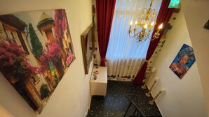 A hotel corridor with a staircase, a painting of a pink car, a chandelier, and a door with an exit sign. - Bonjourla Otel (Urla)