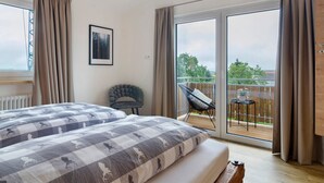 A bedroom with a large bed, a chair, a balcony with a table and chairs, and a view of greenery. - Apartment 'Morning Sun' with Shared Garden and Wi-Fi (Donaueschingen)