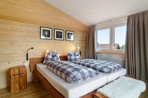 Une chambre à coucher aux murs lambrissés, avec un lit, des tables de chevet et une fenêtre avec des rideaux.