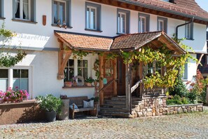A traditional building with a stone staircase, a wooden bench, and a covered porch with plants.