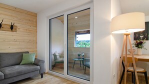A modern living room with a sofa, a dining table with chairs, a lamp, and a large sliding glass door leading to an outdoor area. - Holiday Apartment 'Sternenhimmel' with Shared Garden, Balcony and Wi-Fi (Donaueschingen)