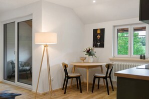 A modern kitchen with a dining area, a floor lamp, and a view of greenery outside.
