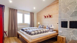 Un dormitorio con una cama de madera, una pared de piedra, un ventanal con cortinas y una chimenea de piedra.