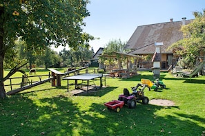 Un espace extérieur verdoyant avec une table en bois, un coin salon abrité et un tracteur.