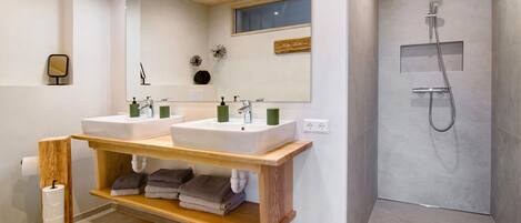 A modern bathroom with two sinks, a mirror, a shower, and wooden shelves.
