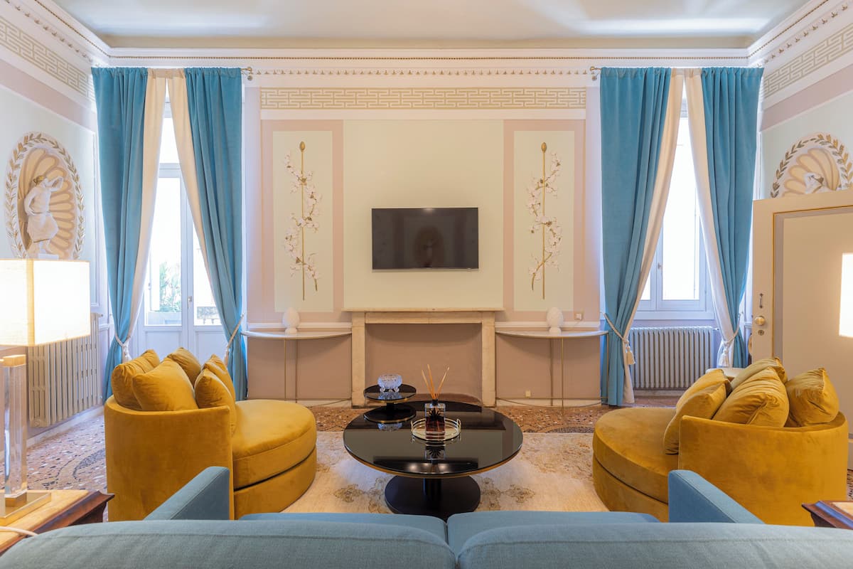 Una sala de estar con chimenea, dos sillones amarillos, un sofá azul y un televisor montado en la pared.
