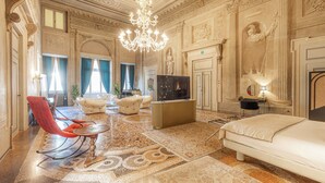 A luxurious hotel room with a large bed, a red chair, a TV, and ornate wall decorations. - Corte Realdi Suites Palazzo Camozzini (Verona)