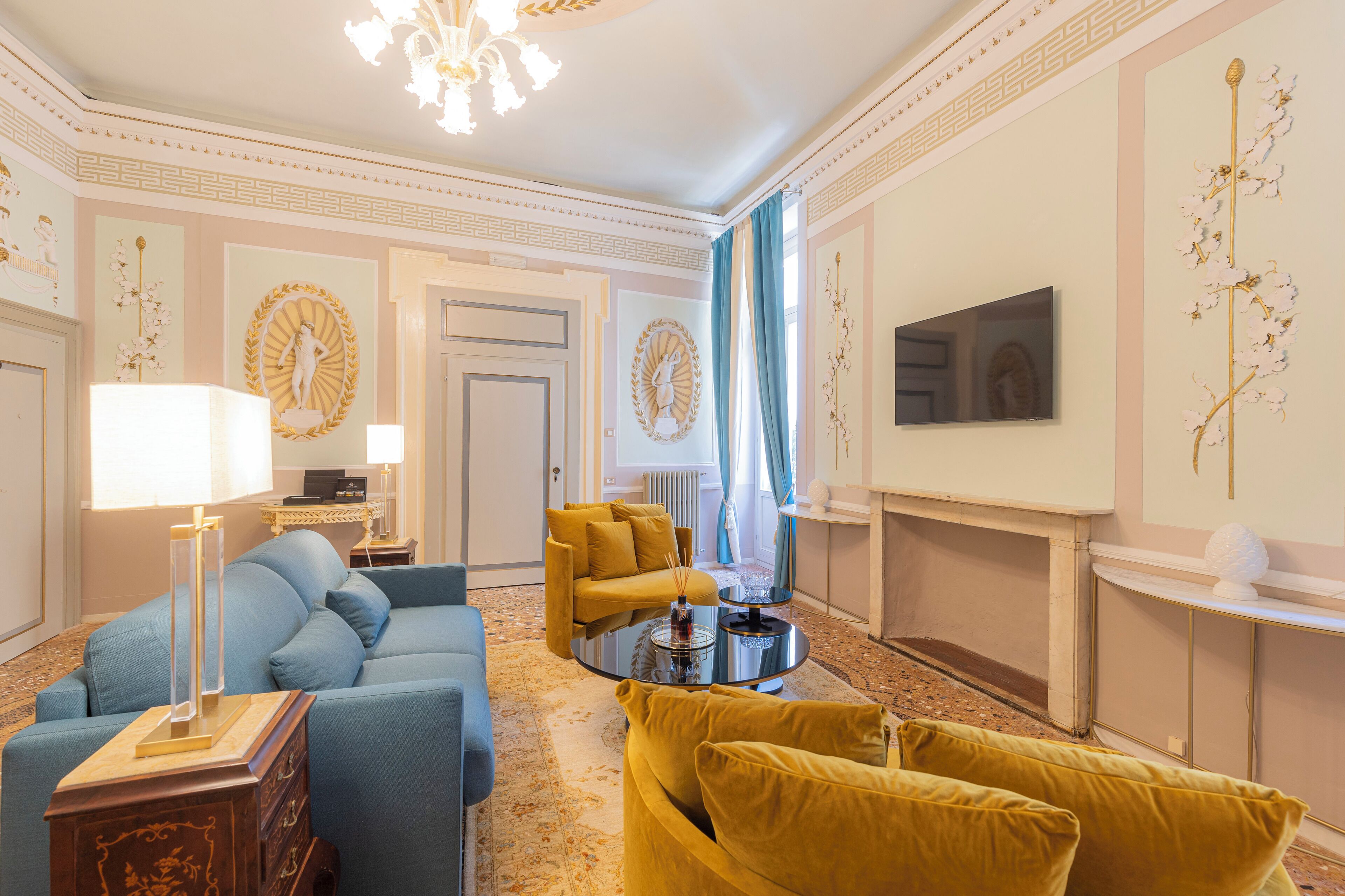Een stijlvol ingerichte woonkamer met een blauwe bank, een gele fauteuil en een glazen salontafel.