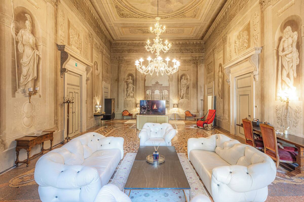 Una habitación lujosa con un amplio sofá blanco, una araña y decoraciones ornamentales en las paredes.