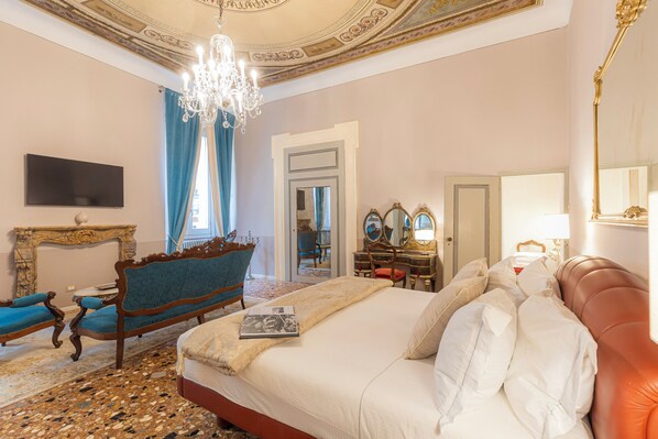 Un dormitorio lujoso con una cama grande, un chaise lounge, un tocador con espejos y una araña.