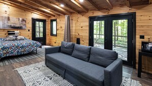 Un interior de cabaña acogedor con un sofá gris, un tapete estampado y una cama con colcha floral.