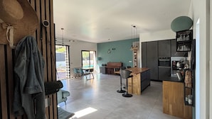 A modern kitchen with a central island, a dining area with a piano, and a view of the outdoors.