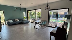 A modern living room with a sectional sofa, a dining table with chairs, and large sliding glass doors leading to an outdoor patio.