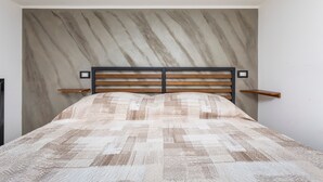 Een bed met een gebedruid sprei, een hoofdbord met horizontale latten, en twee nachtkastjes met wandlampen.