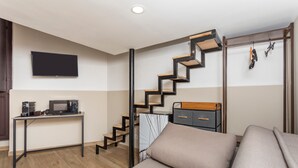 Een functionele leefruimte met een kitchenette, een aan de muur bevestigde televisie, een trap met houten details en een bank.