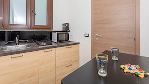 Een keuken met een magnetron, fornuis en kastjes. Er staan twee glaasjes op tafel.