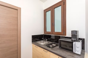 A compact kitchen with wooden cabinets, a microwave, a coffee maker, and a sink.