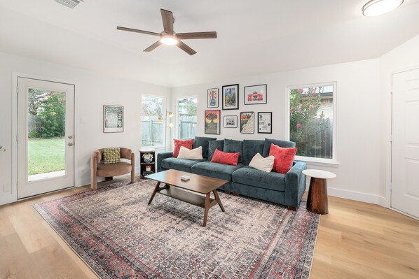 A living room with a sofa, coffee table, and a rug. There are pictures on the wall and a ceiling fan. - Cozy North Austin Getaway  Peaceful  Near Domain (Austin)