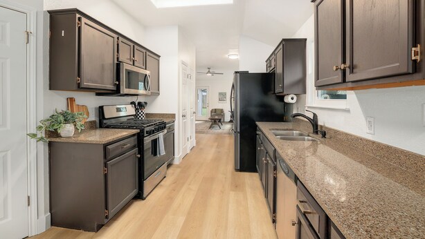A kitchen with dark wooden cabinets, a granite countertop, a black refrigerator, and a microwave.