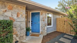 A house with a stone exterior, a blue door, a wooden fence, and a welcome mat.
