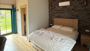 Une chambre avec un plafond en bois, un mur en pierre, un lit recouvert de draps blancs, une table de chevet et une vue par la fenêtre.