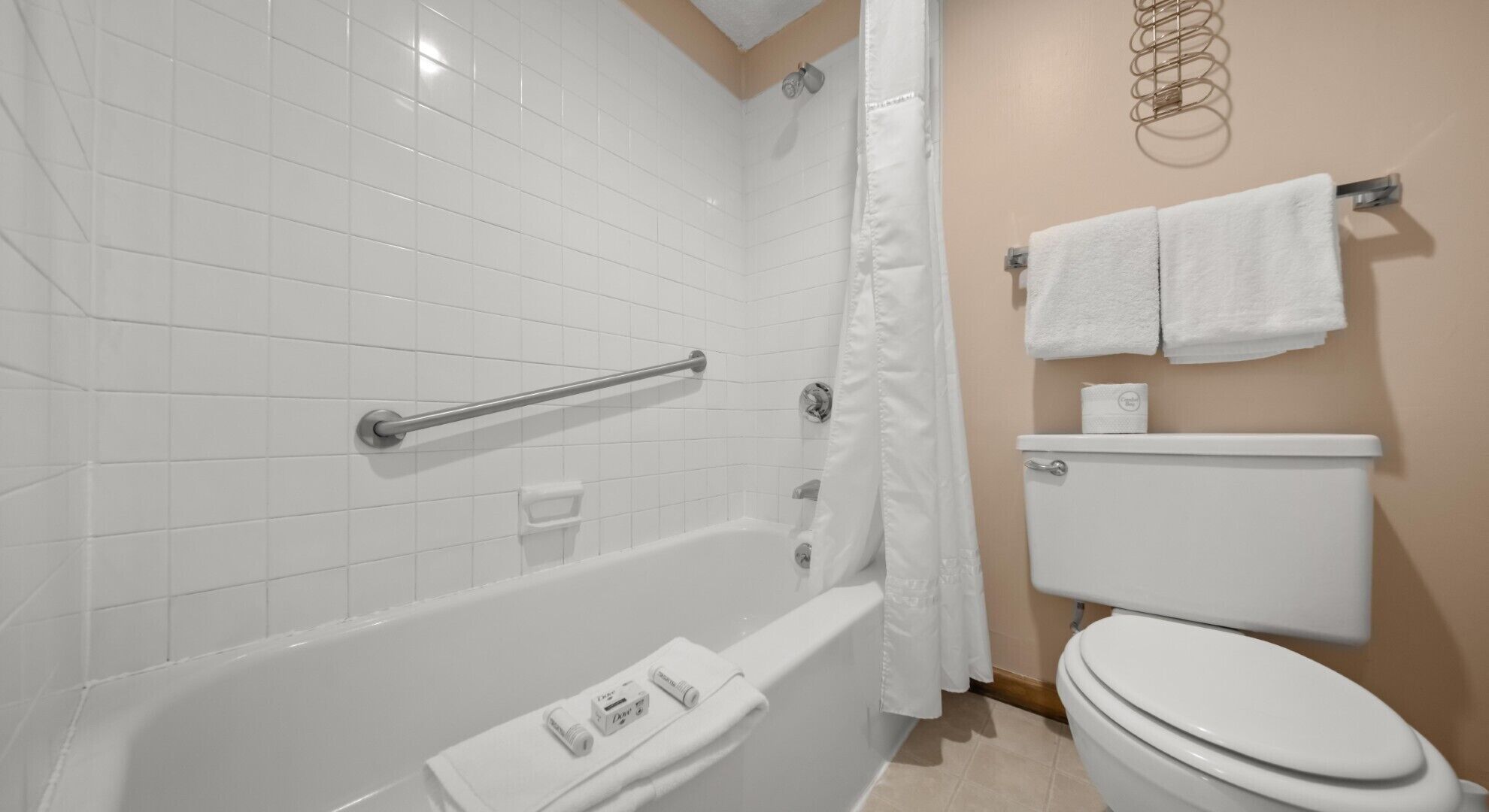 Un baño con paredes de azulejos blancos, una bañera, un cortinón de ducha, un inodoro y un perchero con dos toallas.