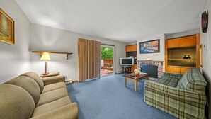A living room with a sofa, a television, a fireplace, and a sliding glass door leading to an outdoor area. - Mountain Magic | 2BR Condo w/ Balcony & Fireplace (Stoneham)