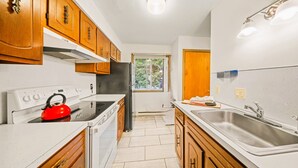 A compact kitchen with wooden cabinets, a stainless steel sink, and a red kettle on the stove. - Mountain Magic | 2BR Condo w/ Balcony & Fireplace (Stoneham)