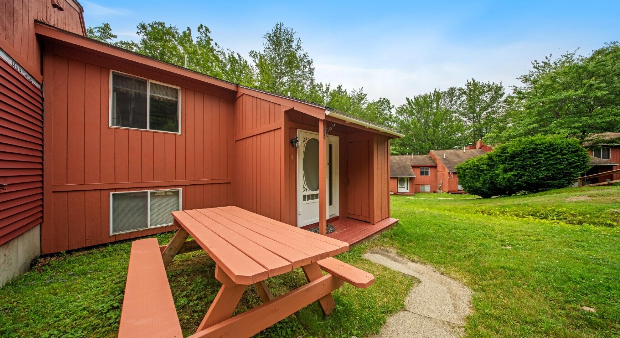A red building with a picnic table in front, a door, and a small garden area.