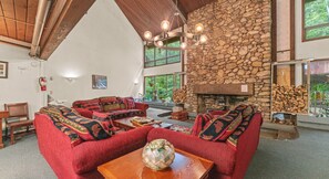 A cozy living room with a stone fireplace, red upholstered furniture, and a large window overlooking greenery. - Cozy Cabin Vibes | 1BR White Mountain Getaway (Stoneham)