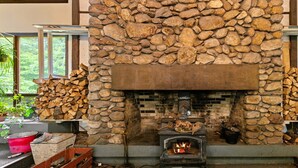 Une cheminée en pierre avec un feu crépitant, entourée de bois de chauffage empilé et agrémentée d’un décor intérieur rustique.