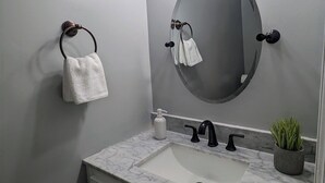 A bathroom with a marble sink, a round mirror, and a towel rack.