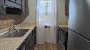 A kitchen with granite countertops, stainless steel appliances, and a window with a white curtain.