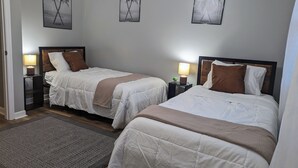 Ein Hotelzimmer mit zwei Betten, jeweils mit Kopfteil, Nachttischen inklusive Lampen und gerahmten Kunstwerken an den Wänden.