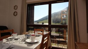 Zona pranzo con tavolo apparecchiato per due, vista su un paesaggio montuoso attraverso ampie finestre e una sedia di legno.