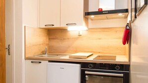 Una cucina compatta con mobili bianchi, forno integrato, lavastoviglie e lampada a sospensione.